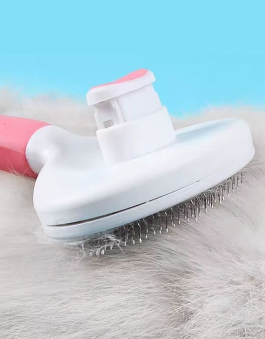 A pet grooming brush with a white body and pink handle, featuring a grid of metal pins, is shown partially inserted into a pile of pet fur, against a blue background.