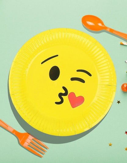 A set of yellow paper plates with a cartoon emoji design, accompanied by orange plastic cutlery, against a green background with decorative stars.