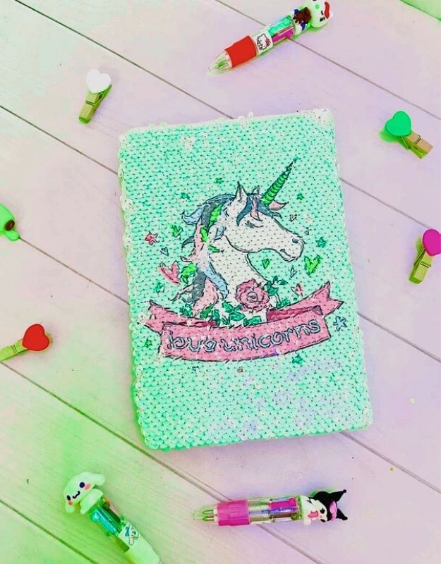 Notebook with unicorn design on a wooden surface with colorful stationery items.