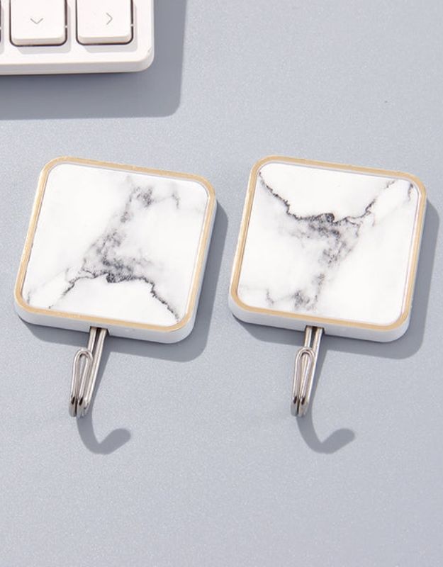 Two square adhesive marble hooks with stainless steel hardware attached to a wall, next to a keyboard for scale.