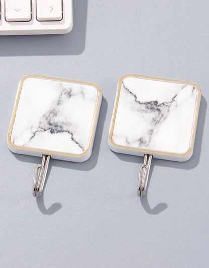 Two square adhesive marble hooks with stainless steel hardware attached to a wall, next to a keyboard for scale.