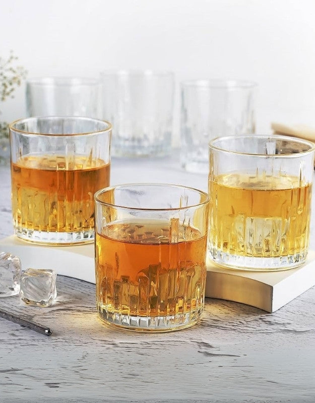 Three glasses of amber liquid on a wooden surface with a blurred background.