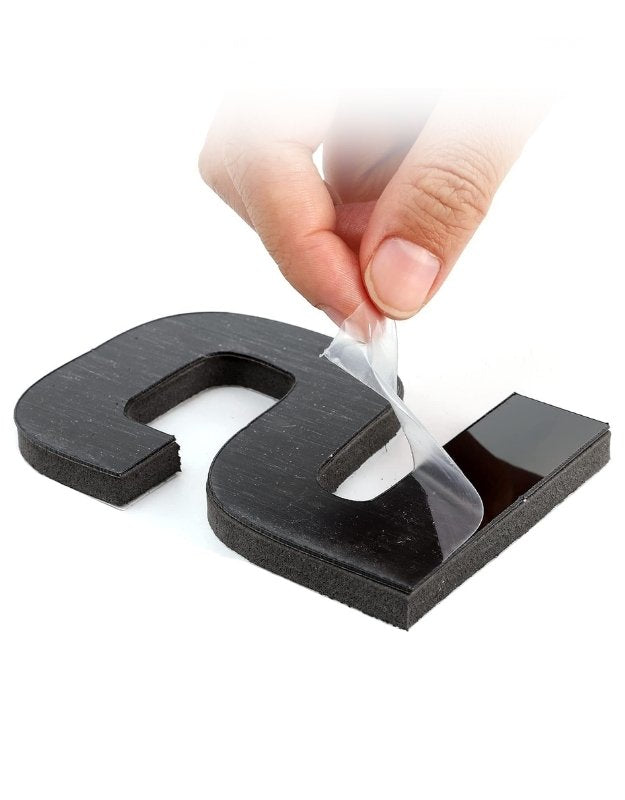 Black U-shaped magnetic piece with hand applying adhesive tape on a white background. Close-up of a hand peeling protective film from adhesive foam number of DIY wall clock.