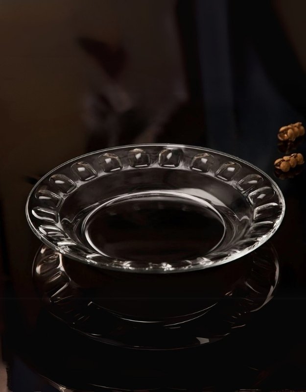 Transparent Kaveh Morvarid platter with textured edge, displayed on a dark reflective surface