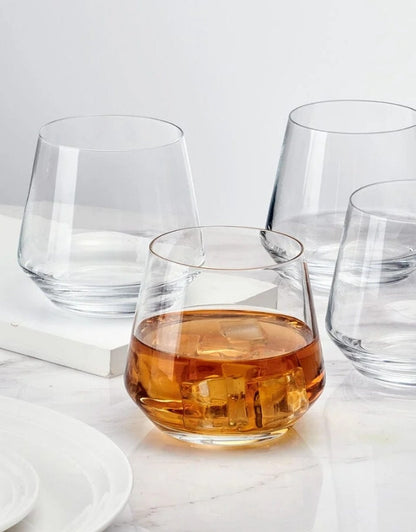 Clear glass with amber liquid on a white surface. Clear whiskey glasses set with one filled with amber drink and ice cubes on marble table.