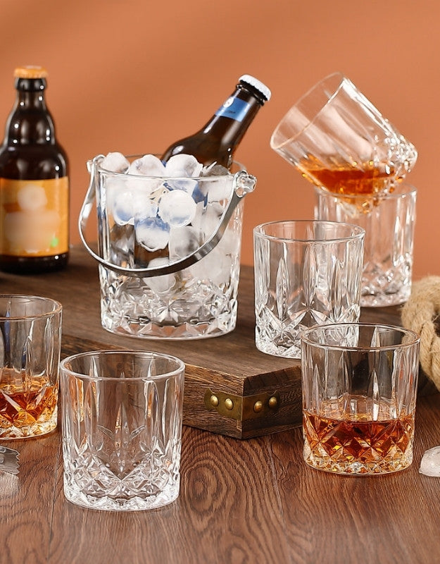 A complete 7-piece crystal glass set with whiskey cups and a patterned ice pail filled with ice and a beer bottle.