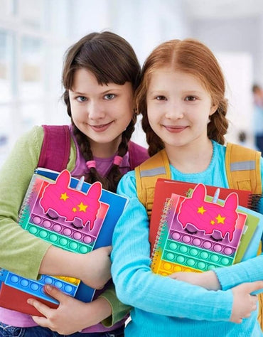 Two smiling girls holding colorful A5 unicorn popit notebooks, ideal for school, play, and creativity.