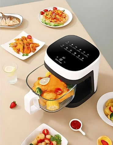 Air fryer on a table with plates of food and a glass of water. Large capacity 8.5L glass air fryer with touch controls, surrounded by cooked meals on a dining table.