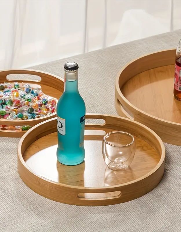 Bottle of blue liquid and glass on a wooden tray. Round bamboo serving trays with drinks and glassware on table.