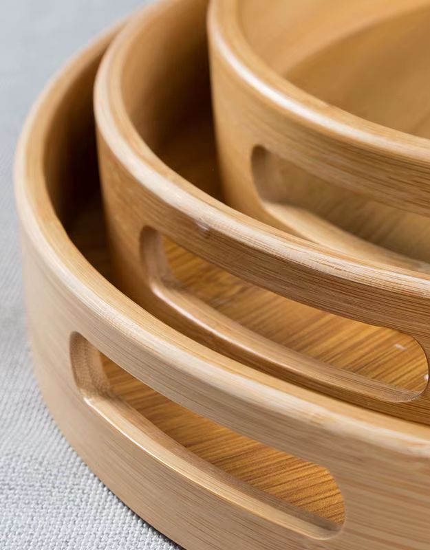 Stack of three bamboo bowls on a light fabric background. Detail of bamboo serving tray handles showing smooth cutouts.
