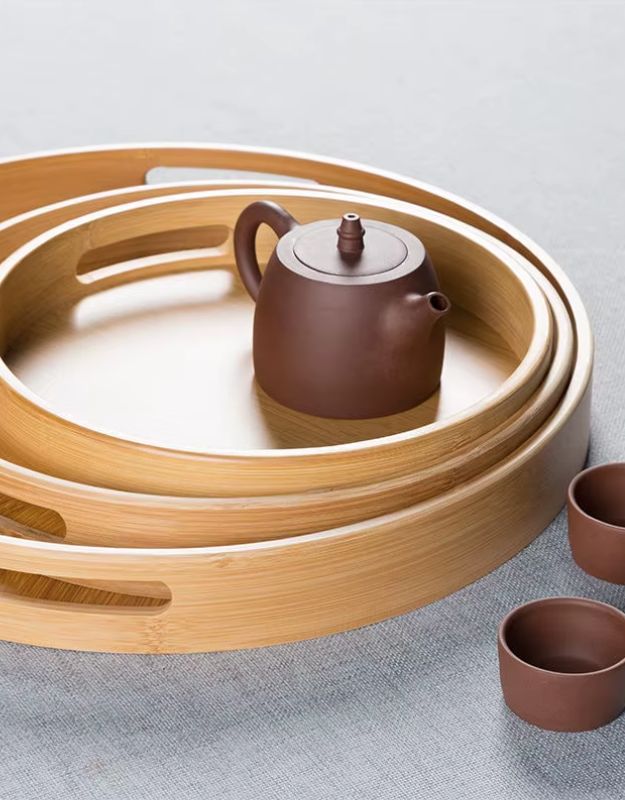 Brown teapot and cups on a wooden tray. Stacked round bamboo serving trays with teapot and cups
