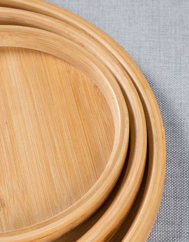 Stack of wooden trays on a textured surface. Close-up of round bamboo serving tray set with smooth finish.