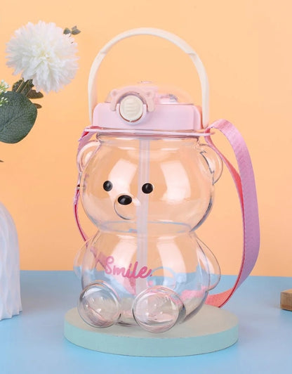 Bear-shaped water bottle filled with water and displayed on a table with pink lid and strap.