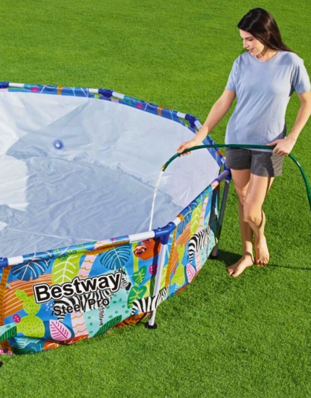 Woman filling Bestway Steel Pro Jungle 305x66cm above-ground pool with water using a garden hose.