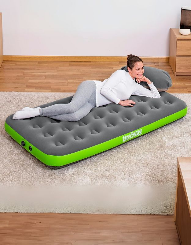 A person lying on a green and gray Bestway Roll and Relax Air Mattress inside a room.