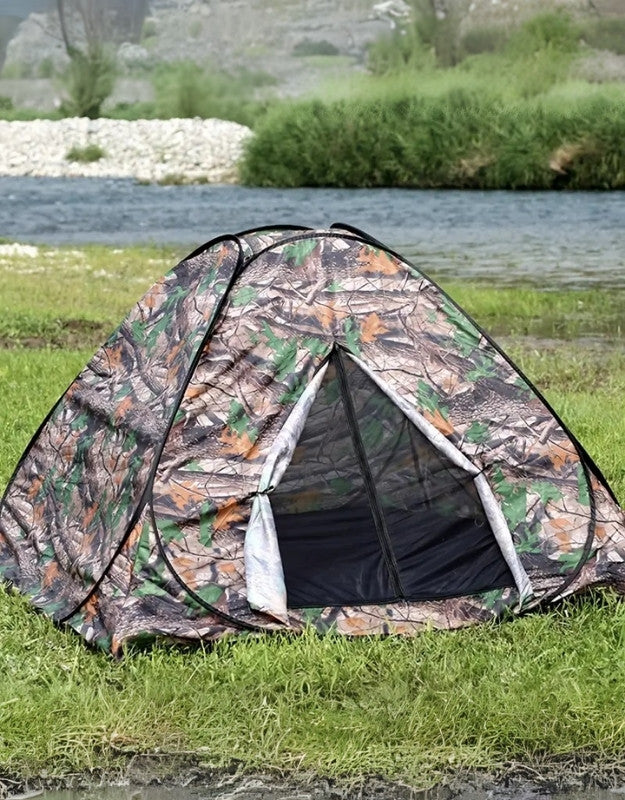 A camouflage camping tent set up on grassy terrain near a body of water.