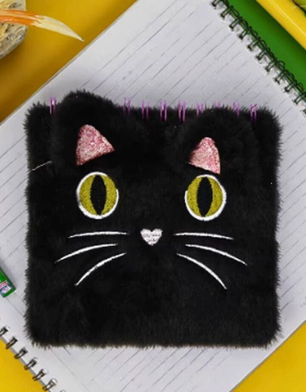 Black cat-shaped pouch with pink ears and yellow eyes on a notebook background