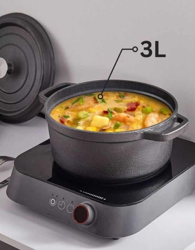 Black pot with food on a hot plate, labeled '3L', on a light gray background. Black cast iron cooking pot with 3-liter capacity, filled with soup on an induction cooktop.