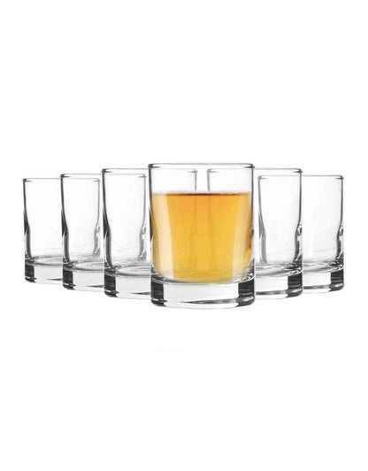 Set of clear glasses with one containing a yellow liquid on a white background.