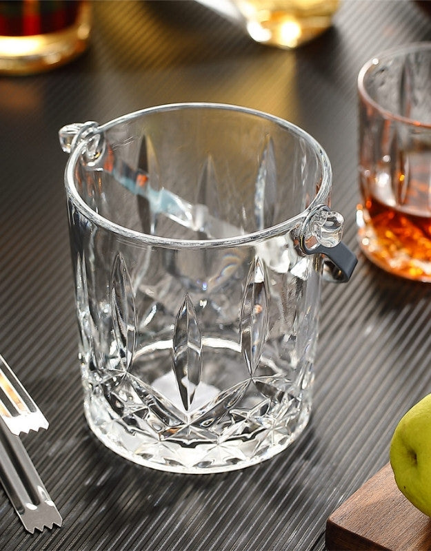 Close-up of an empty crystal ice pail with cut-glass patterns and metal handles on a black table.