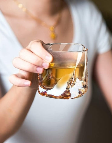 Hand holding a glass of amber liquid against a blurred background.