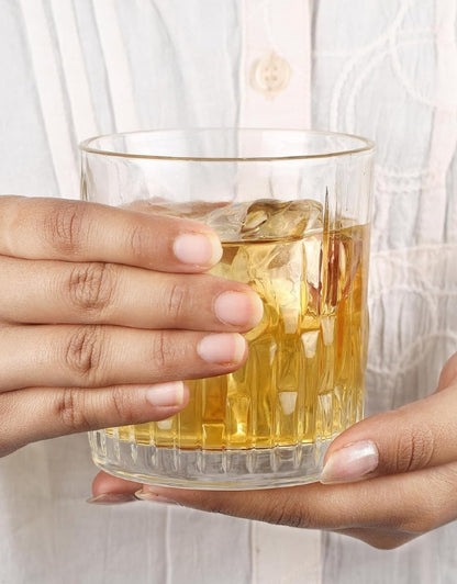 Hand holding a glass of whiskey with ice cubes against a light background.