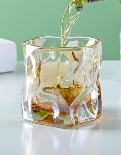 Glass being filled with a clear liquid on a light surface with a green background.
