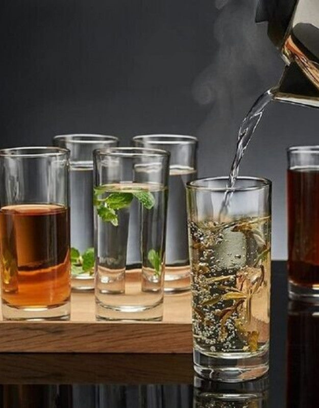 Glassware with different drinks on a wooden surface, including a glass being filled with liquid.