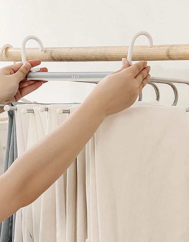 Hands placing beige pants on double hook multi-layer hanger.