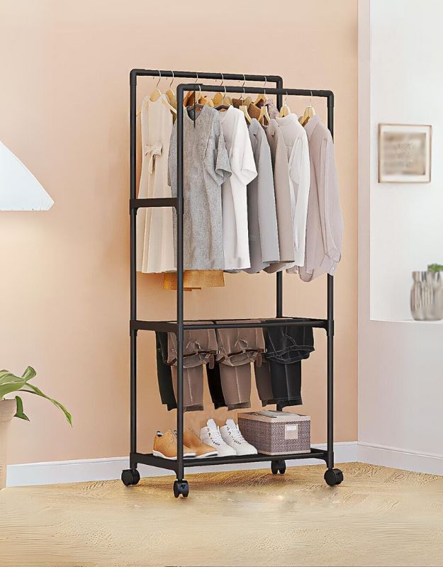 A mobile clothes hanging rod with three tiers of storage space, containing clothes and placed on wheels for mobility, positioned in a room corner.