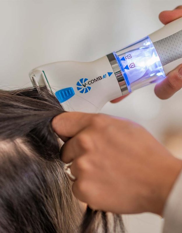 Person using a hair care device on their hair. Electric lice comb V-Comb in use removing head lice and nits from hair.
