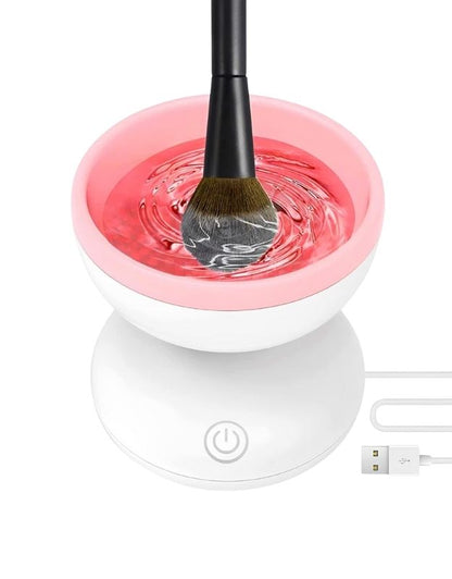 A makeup brush being cleaned in a portable USB-powered electric brush cleaner with pink and white color scheme.