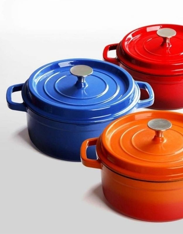 Three colorful cook pots with lids on a light gray background. Set of enamel cast iron Dutch ovens in red, blue, and orange with stainless steel knobs.