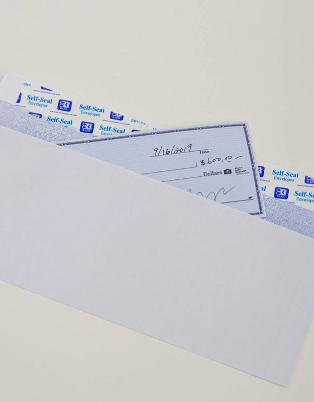 White self-seal envelope with a check partially inserted, showing a dated check with "$600.00" written on it.