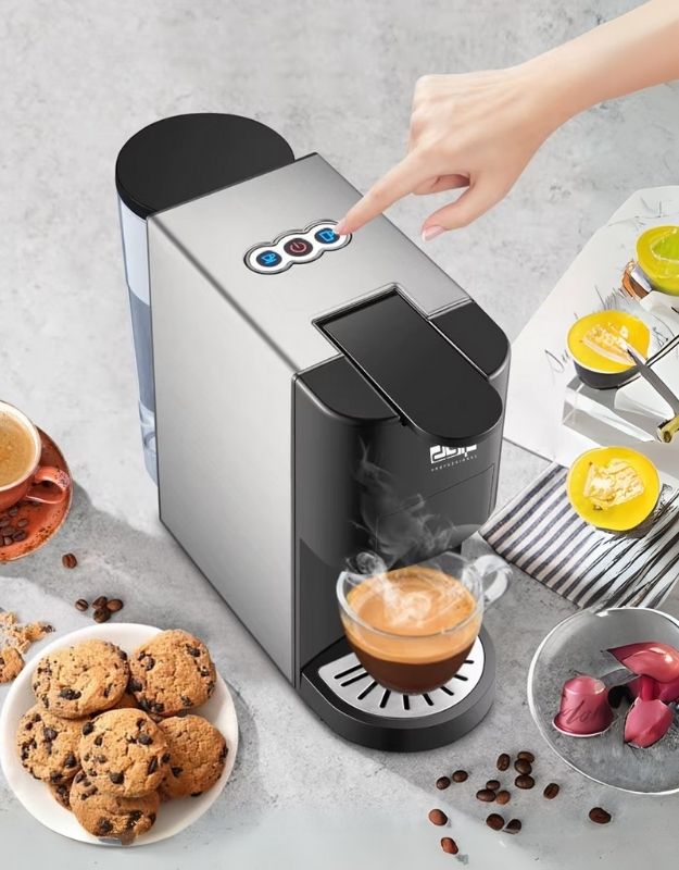 A portable capsule maker 3 in 1 coffee machine with a silver finish, shown making a cup of coffee, surrounded by cookies, coffee beans, and other coffee-making accessories.
