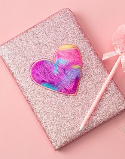 Glittery notebook with a heart-shaped cookie and pink pencil on a pink background