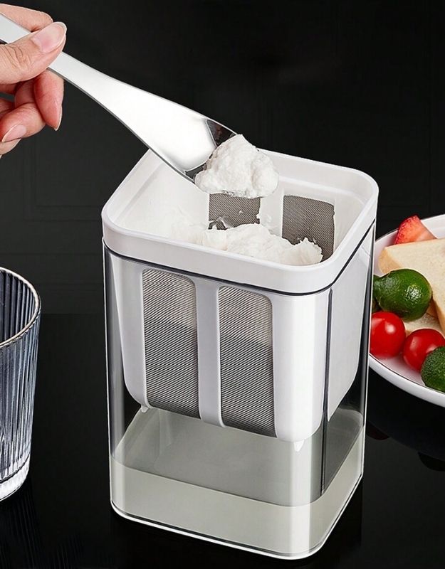 Hand scooping thick strained Greek yogurt from strainer container.