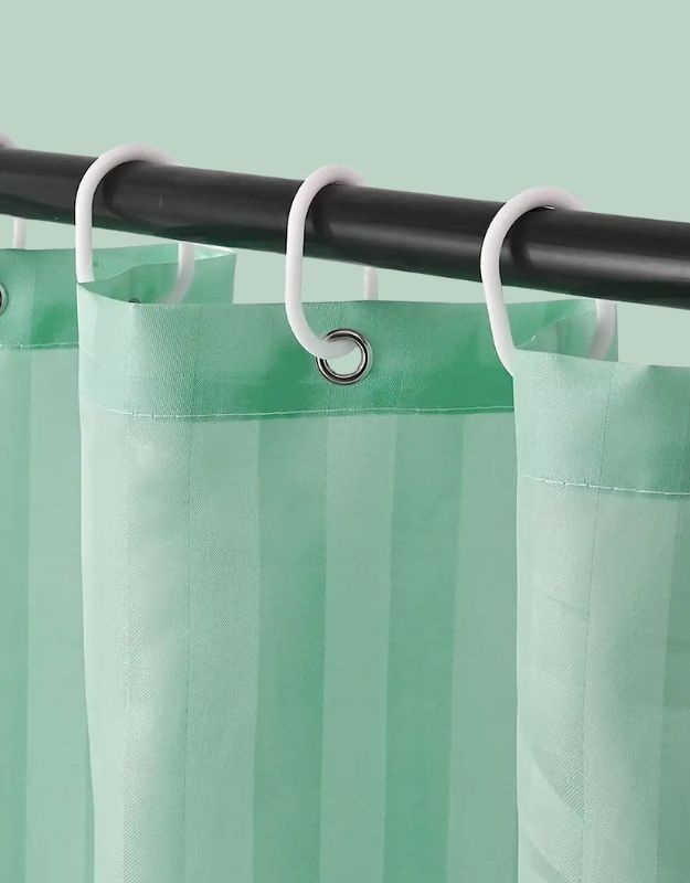 Closeup of green striped shower curtain hanging on rod with hooks.
