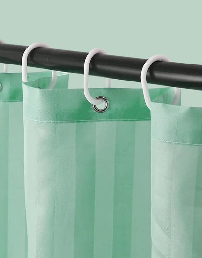 Closeup of green striped shower curtain hanging on rod with hooks.