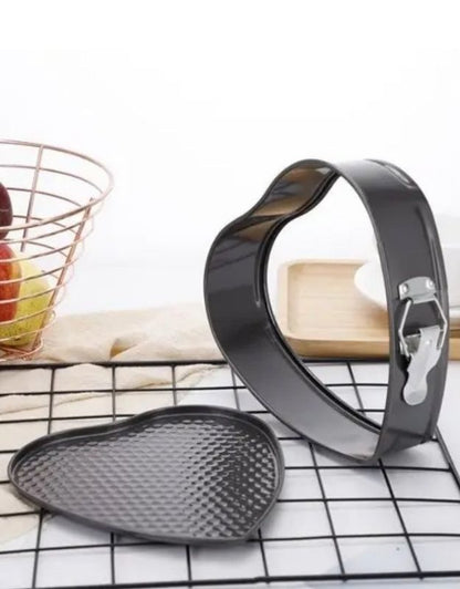 Metal cookie cutters on a cooling rack with a kitchen background. Heart-shaped springform cake pan with detachable base and latch.