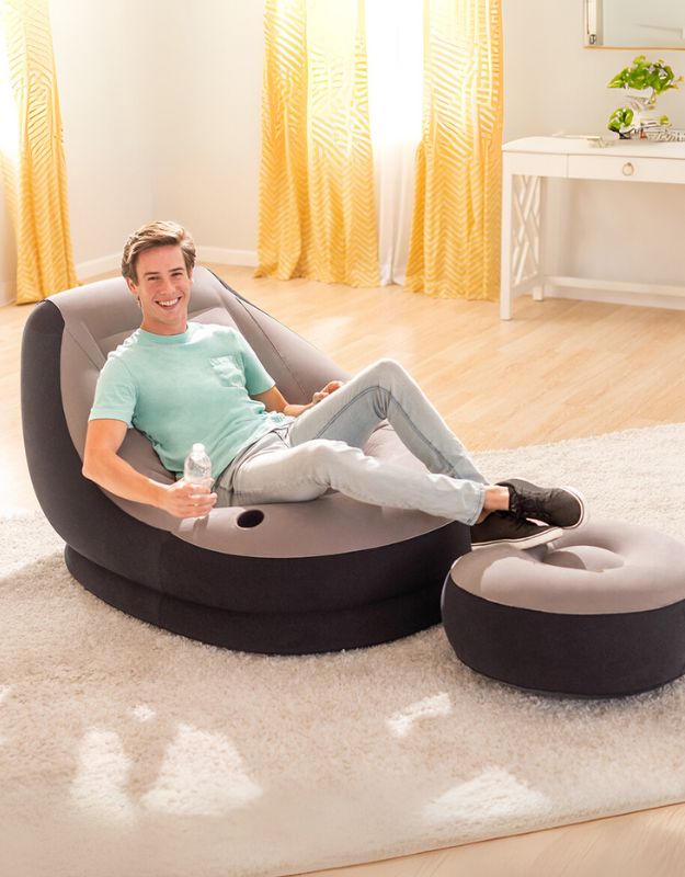 A person sitting relaxedly on an Intex Ultra Lounge inflatable chair with an ottoman by their feet, indoors.