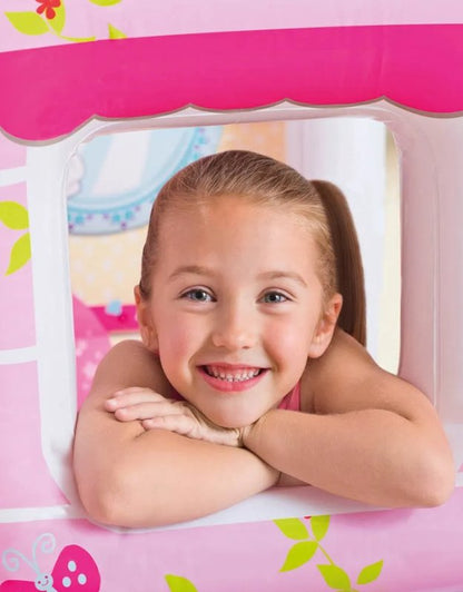 Smiling girl leaning on the window of a pink inflatable playhouse.