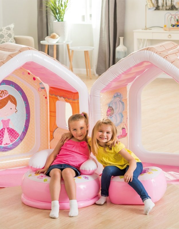 Two young girls sitting on inflatable chairs in front of a pink playhouse.