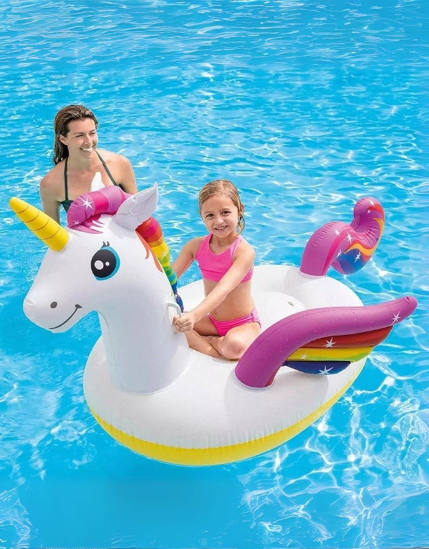 Girl sitting on large inflatable unicorn float with rainbow wings and horn in a swimming pool.