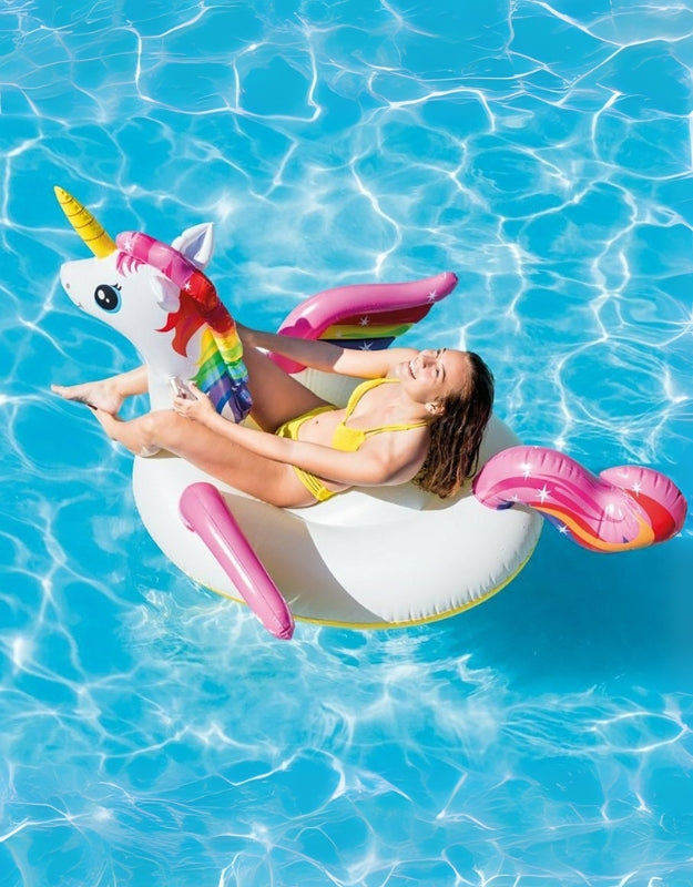 Woman relaxing on giant unicorn pool float with colorful mane and tail in bright blue water.