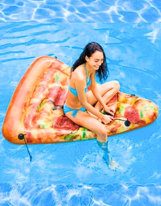 Woman sitting on an inflatable pizza slice float in a swimming pool, smiling in a blue bikini