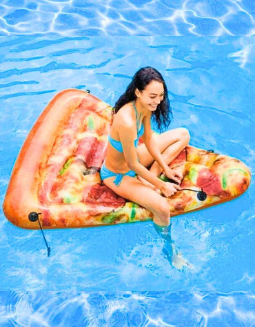 Woman sitting on an inflatable pizza slice float in a swimming pool, smiling in a blue bikini