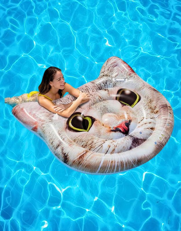 Woman relaxing on an Intex 58784EU hyperrealistic cat face inflatable pool mat with handles, floating on clear blue water.