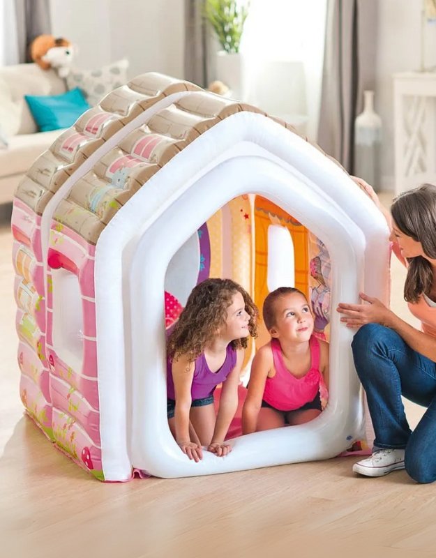 Children playing inside an inflatable house with a pink and white color scheme, featuring a arm chair and ottoman.