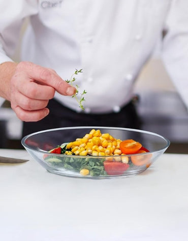 Chef garnishing fresh salad with corn and tomatoes in a clear Kaveh Duralex cocktail plate